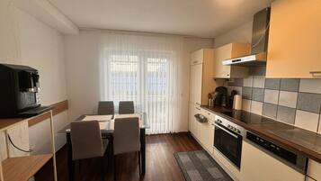 A compact kitchen with a dining table, chairs, a coffee machine, and a stove.