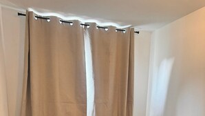 A single bed with a patterned bedspread and two pillows, a wooden floor, and a curtain with a rod. - E&H Appartements  (Bregenz)