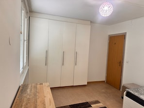 A bedroom with a wardrobe, a bedside table, a bed, a door, and a hanging light fixture. - E&H Appartements (Bregenz)