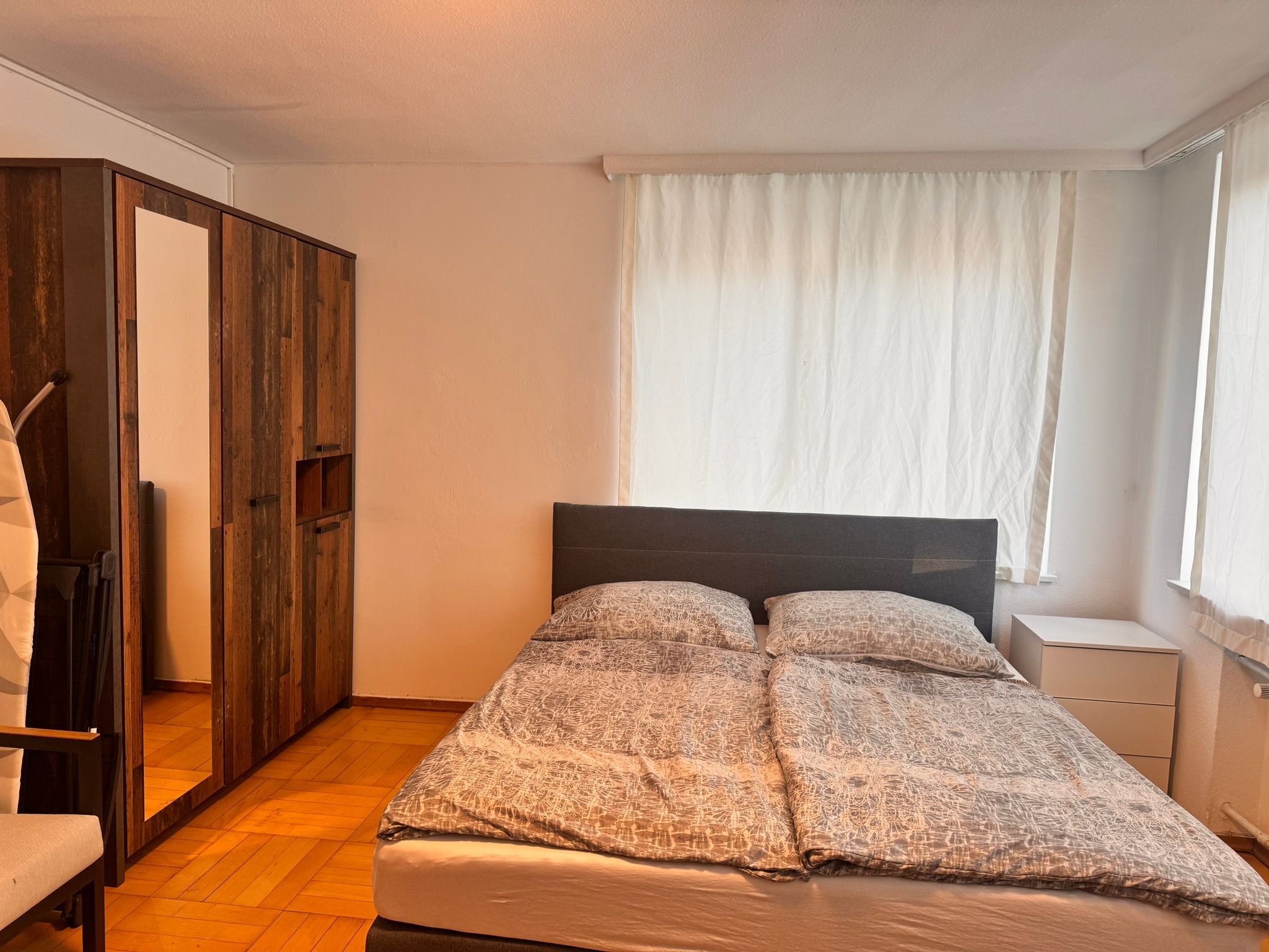 A bedroom with a bed, a wardrobe, and a window with curtains.