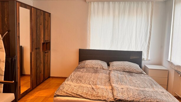 A bedroom with a bed, a wardrobe, and a window with curtains. - E&H Appartements  (Bregenz)