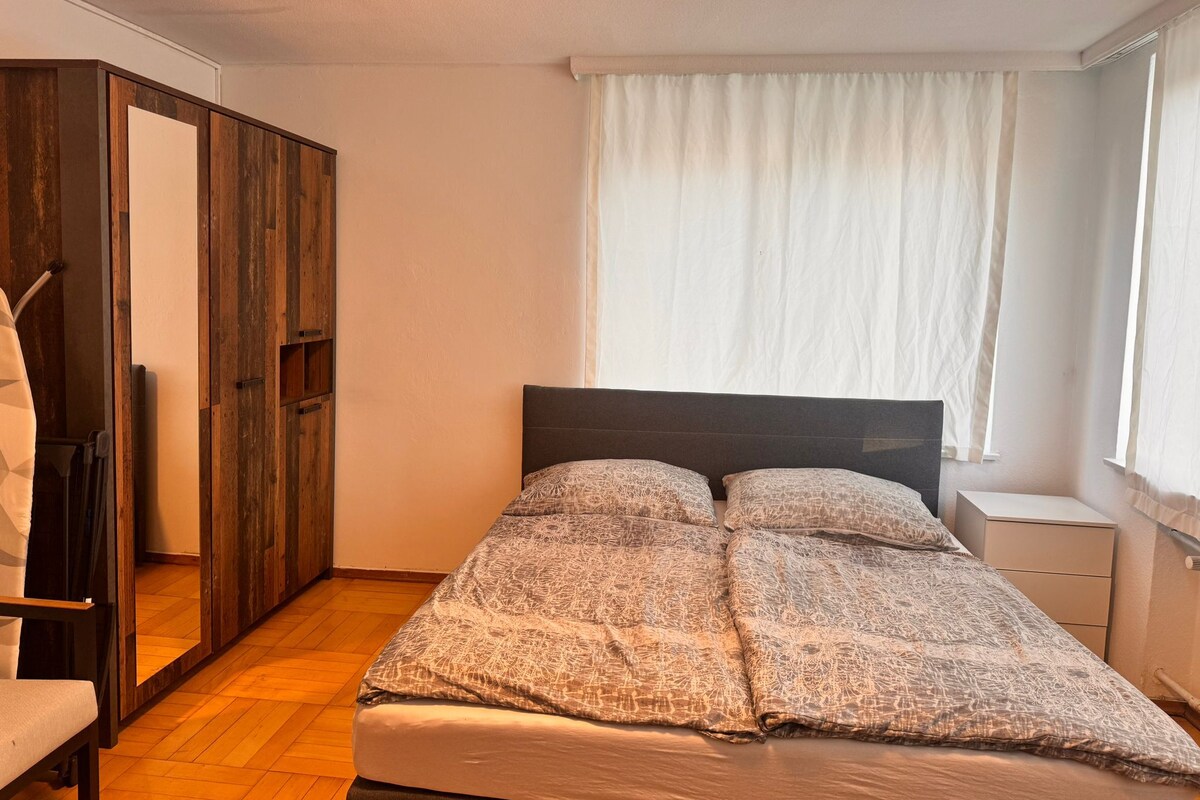 A bedroom with a bed, a wardrobe, and a window with curtains.