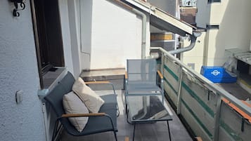 Ein Balkon mit einer Couch und zwei Stühlen, ein Fenster und ein Blick auf ein Gebäude im Hintergrund.