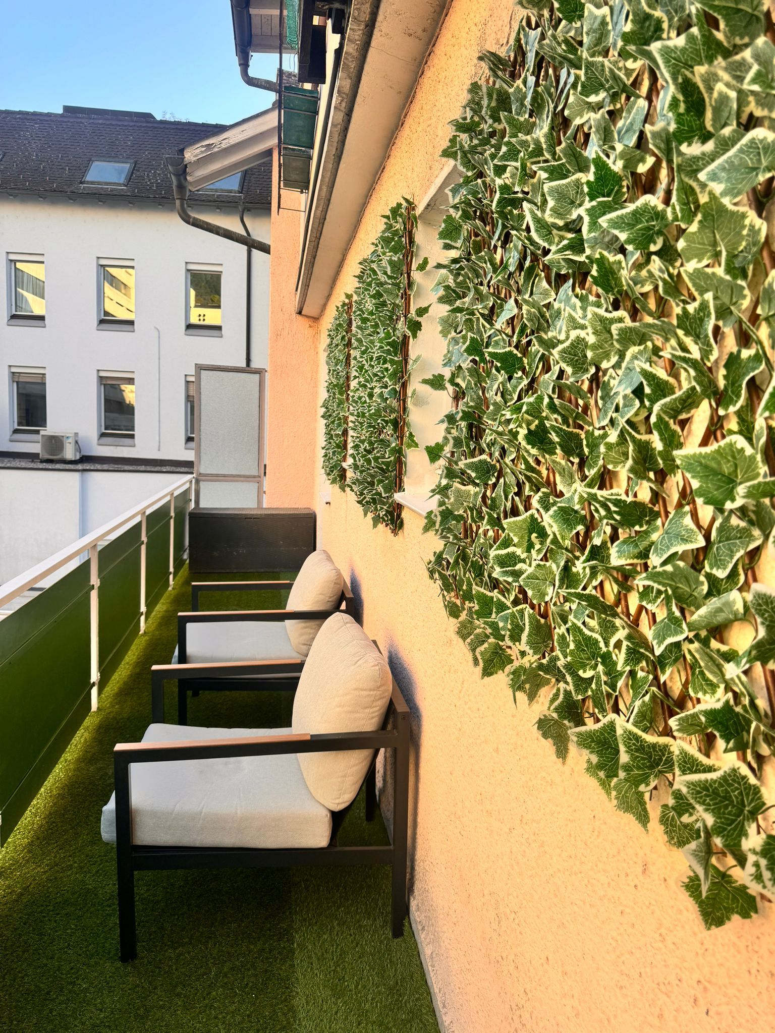 Un balcón con suelo de césped artificial verde, barandilla blanca y pared cubierta de hiedra.