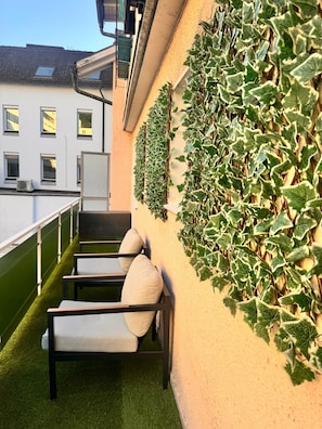 A balcony with a green artificial turf floor, a white railing, and a wall covered with ivy. - E&H Appartements (Bregenz)
