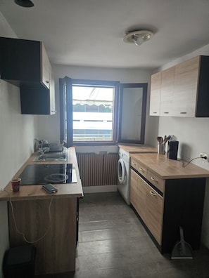A compact kitchen with a built-in washer, a window with a view, and wooden cabinetry. - E&H Appartements (Bregenz)