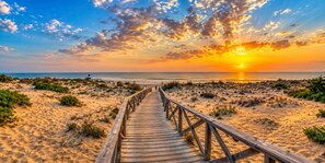 Een houten looppad dat naar een strand leidt, met een zonsondergang op de achtergrond.