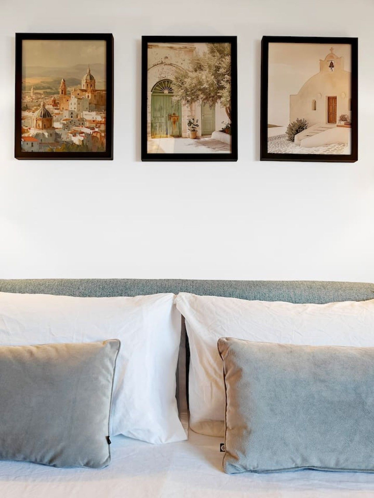 A bed with two pillows and three framed artworks on the wall above.