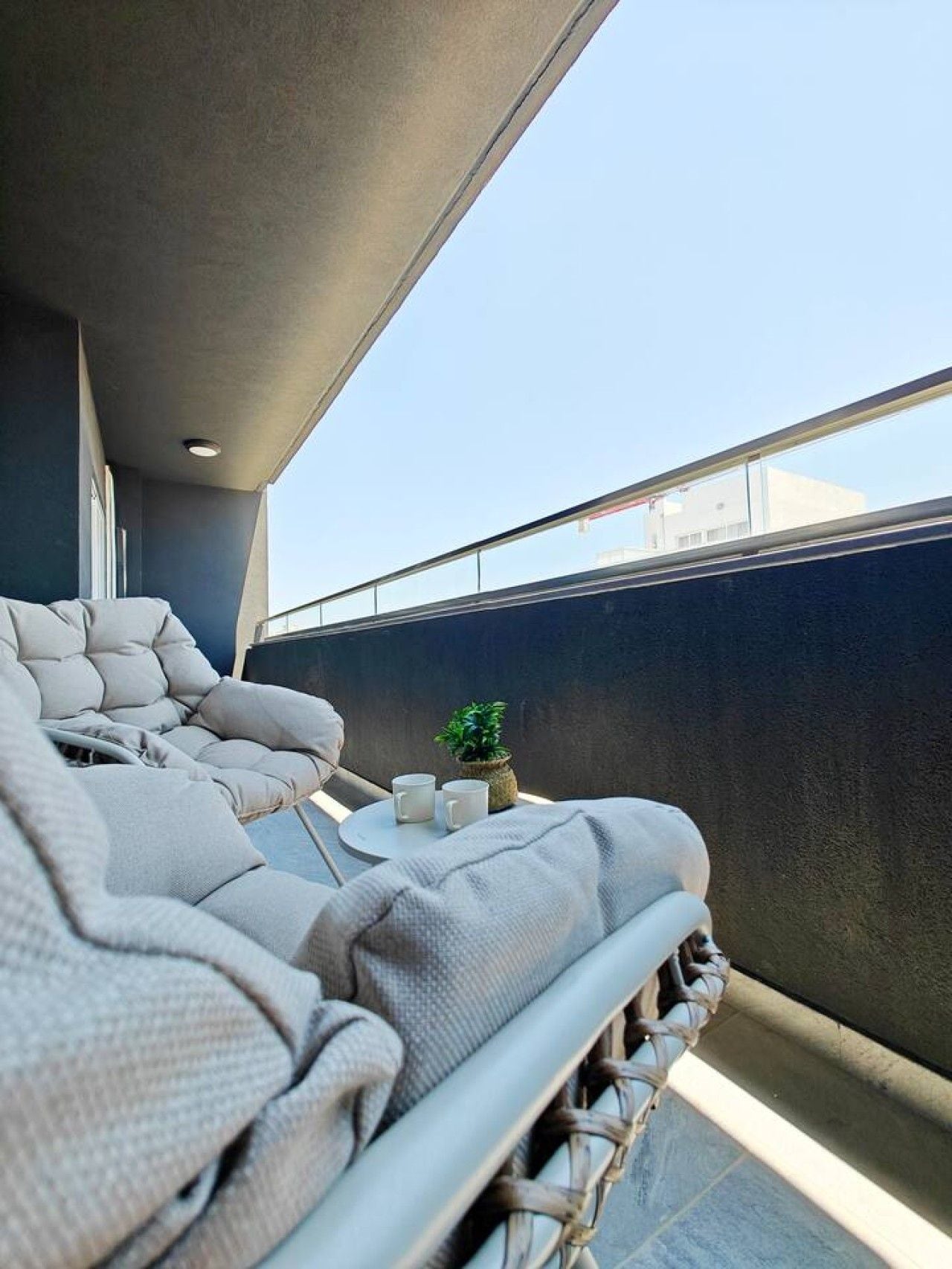 A balcony with a seating area, a small table with two cups, and a potted plant.