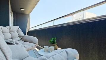 A balcony with a seating area, a small table with two cups, and a potted plant.