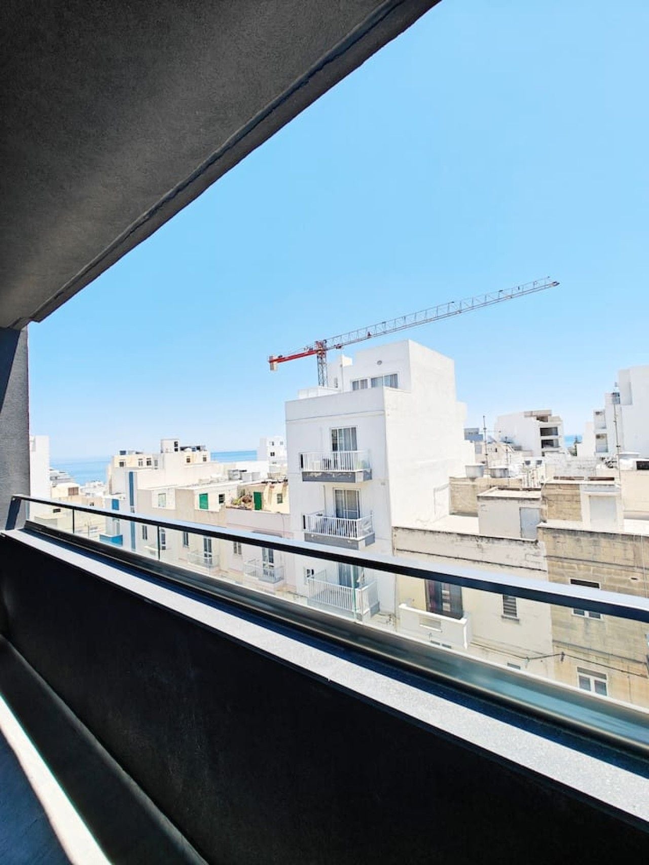 Une vue depuis un balcon, avec un ciel dégagé, une grue de construction et un paysage urbain composé de différents bâtiments.