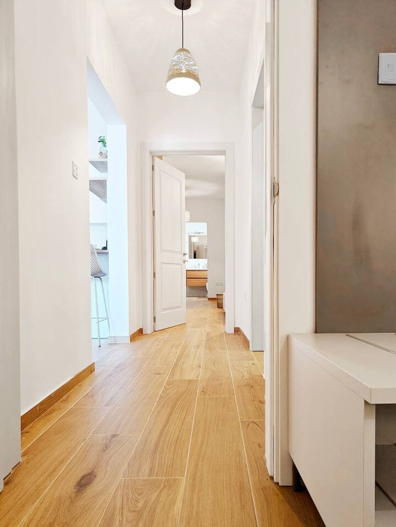 Un couloir doté d’un plancher en bois, de murs blancs et d’un luminaire suspendu.
