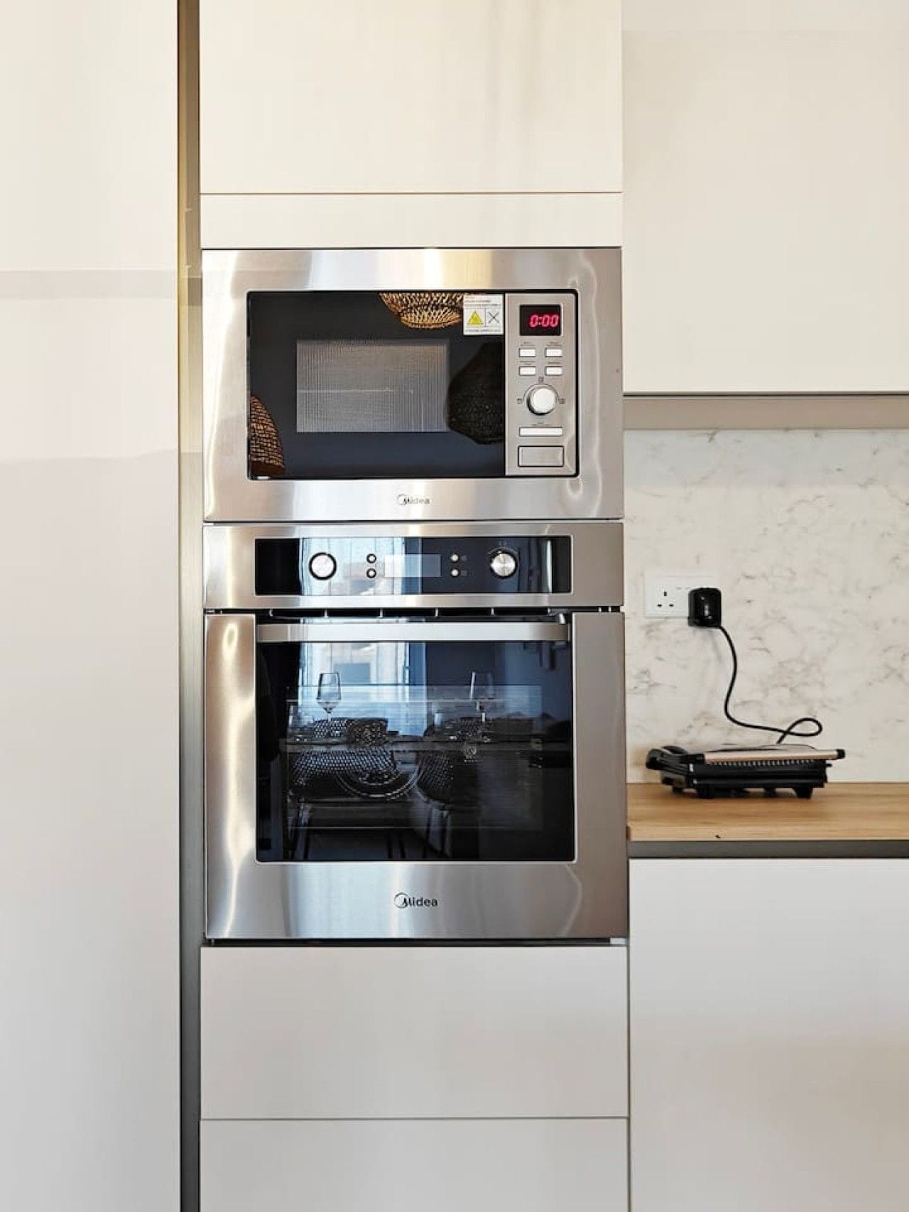 Un horno de acero inoxidable con reloj digital y panel de control, ubicado en una cocina moderna con salpicadero de mármol.