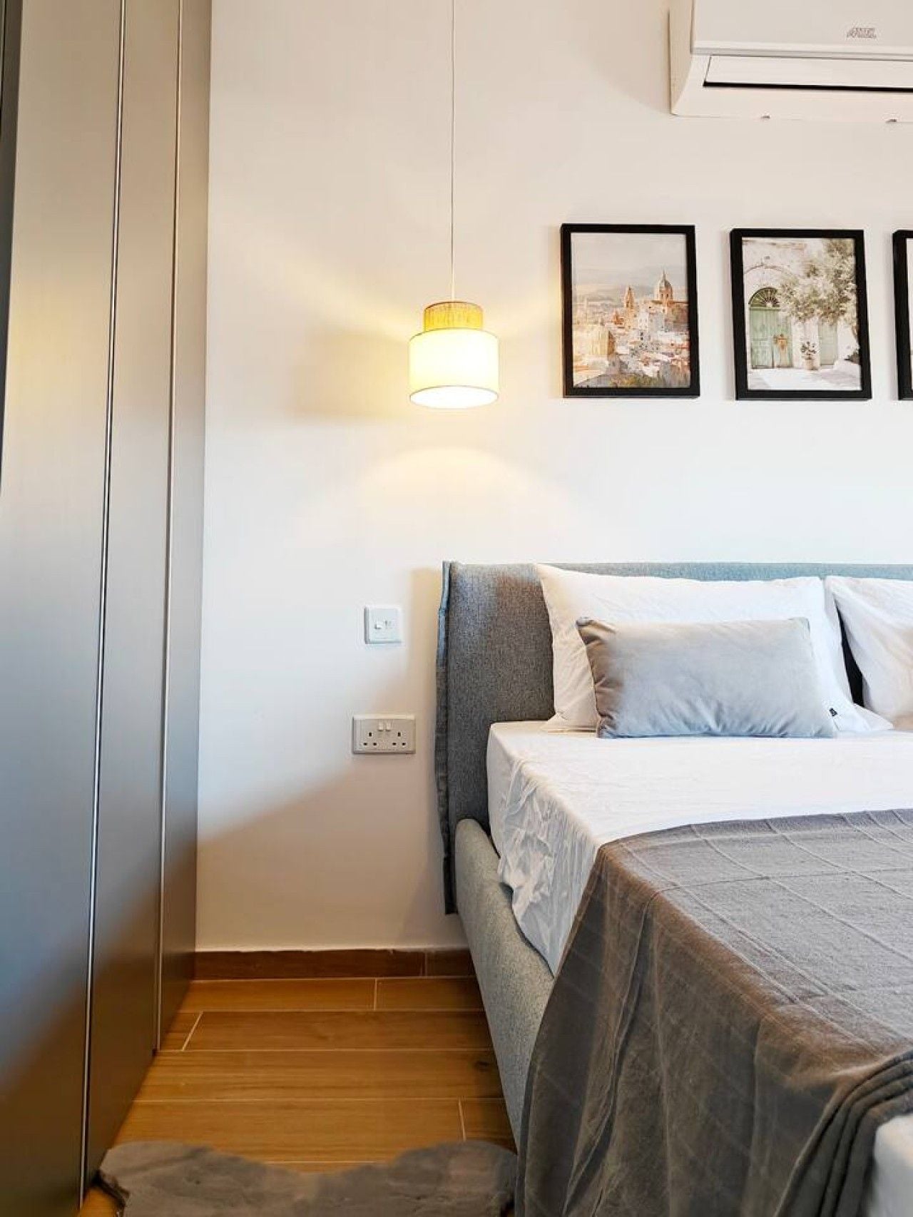 Une chambre à coucher comprenant un lit, un climatiseur fixé au mur, un luminaire et trois tableaux encadrés.