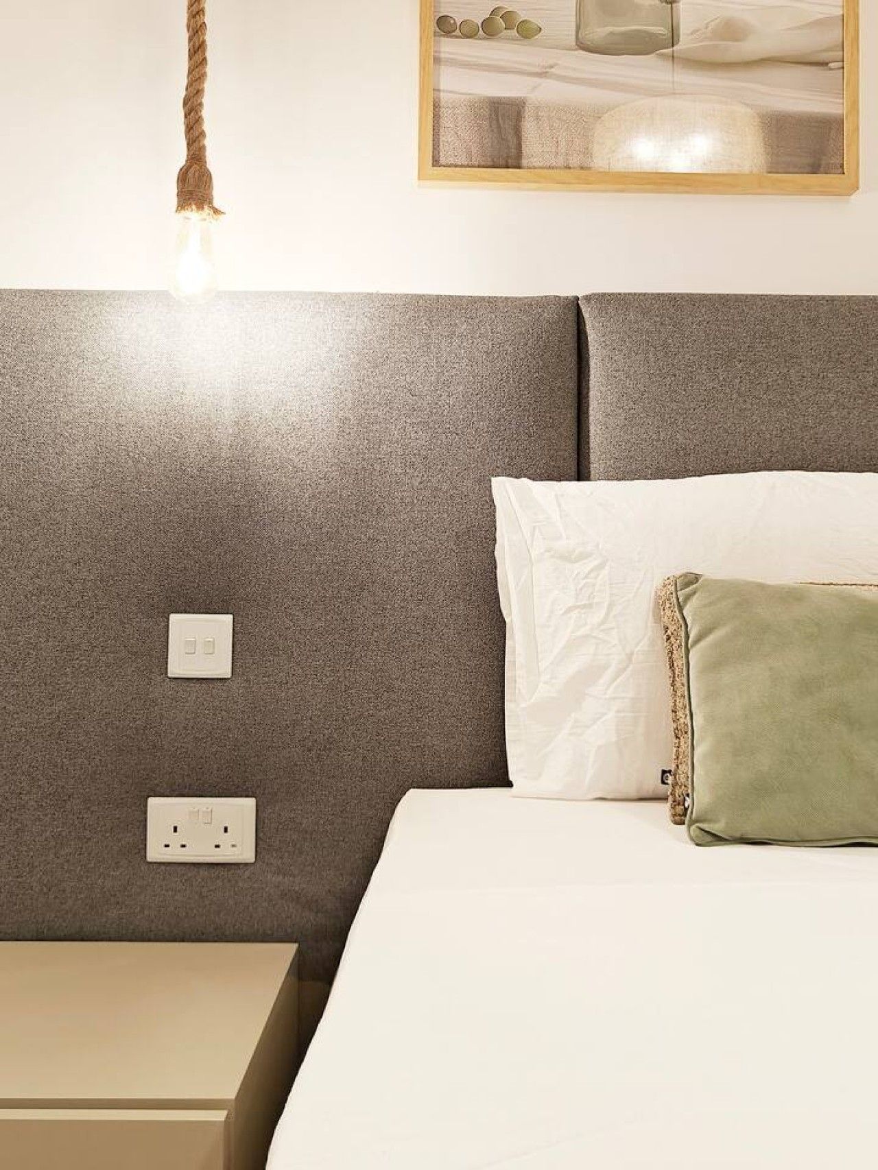 Une chambre à coucher avec une tête de lit, une table de chevet, une lampe et un tableau au mur.