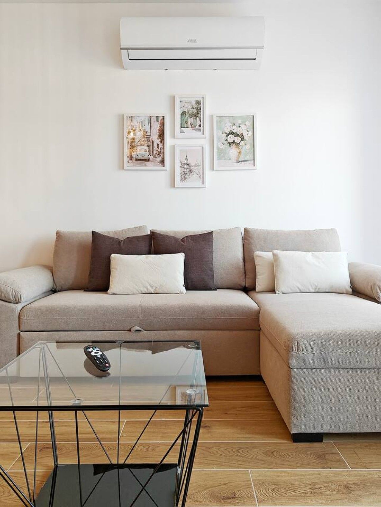 Un salon moderne avec un canapé d’angle, une table basse en verre et un climatiseur fixé au mur.