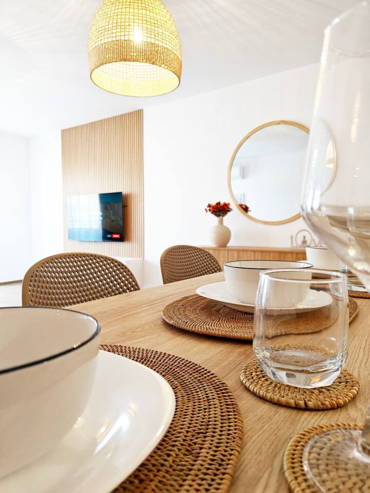 Un coin repas avec une table ronde, des sets de table en fibres naturelles et un luminaire suspendu.