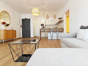 A modern living room with a sofa, a glass coffee table, wicker chairs, a kitchen in the background, and a large mirror. - Marsascala 2 bedroom apartment (Wied il-Għajn)