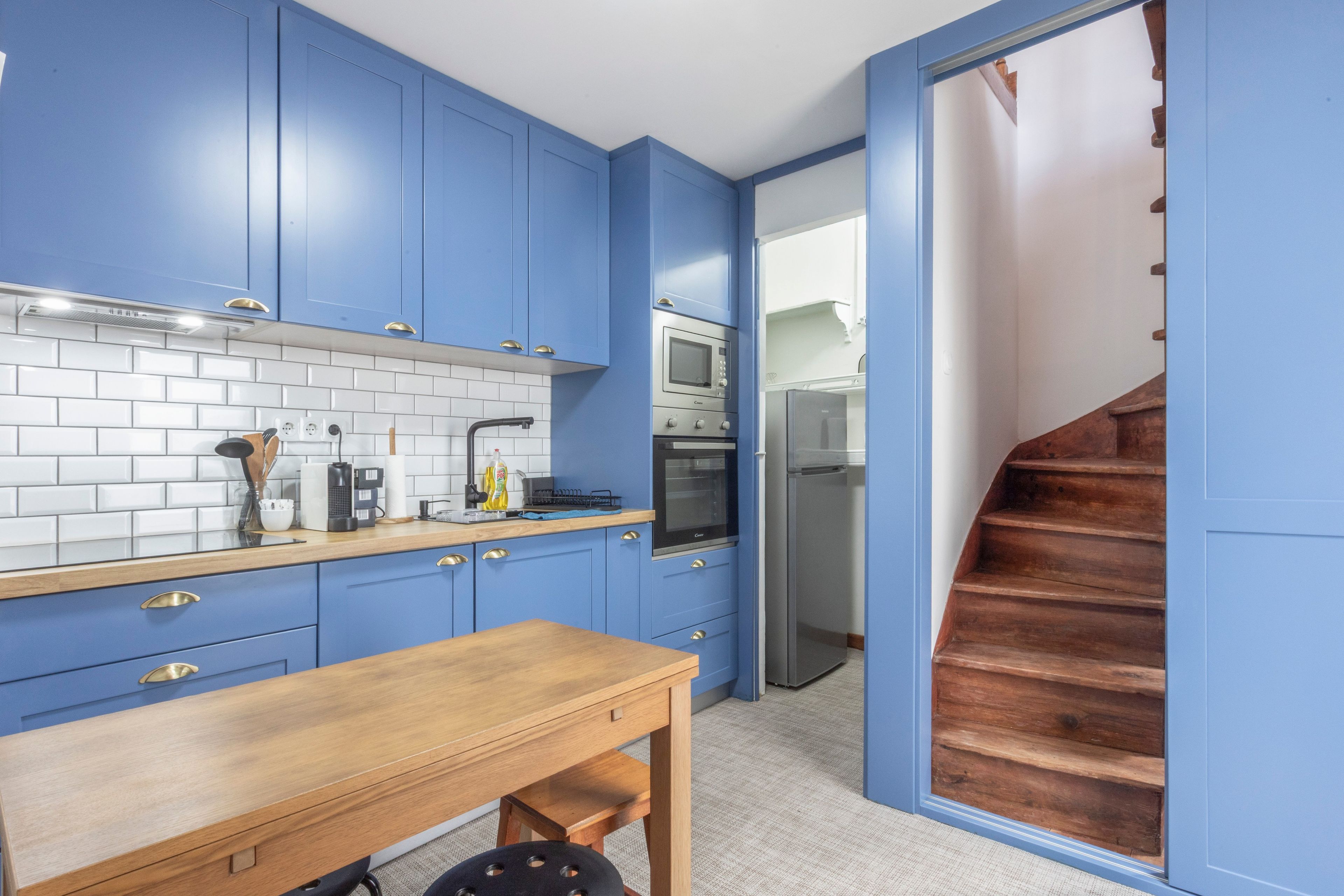 Een keuken met blauwe kastjes, een houten tafel en een oven van roestvrij staal.