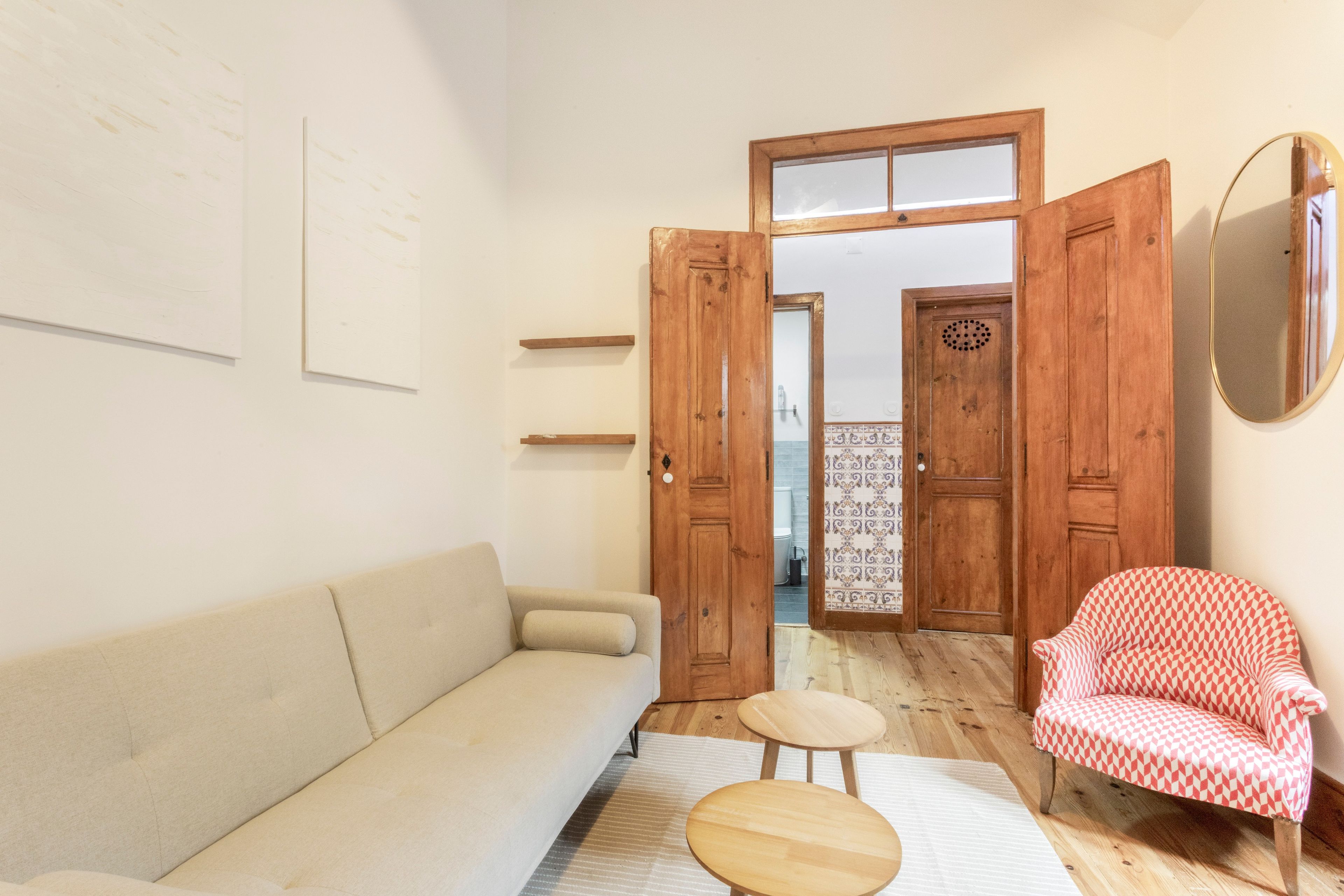 Een kamer met een bank, een stoel, een klein tafeltje en een houten deur naar een badkamer.