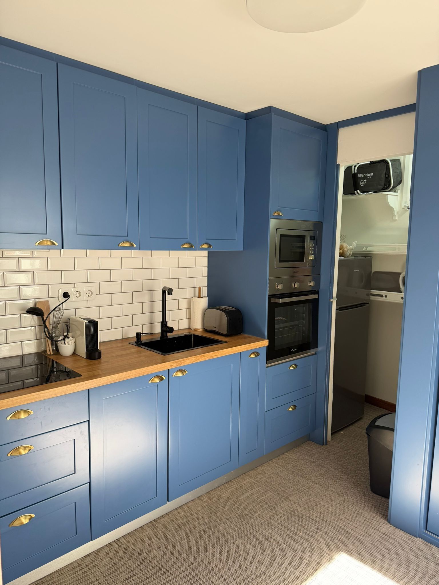 Una cocina compacta con armarios azules, una encimera de madera, un lavamanos, un tostador y un horno integrado.