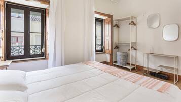 A bedroom with a bed, a bedside table, a mirror, and a window with curtains.