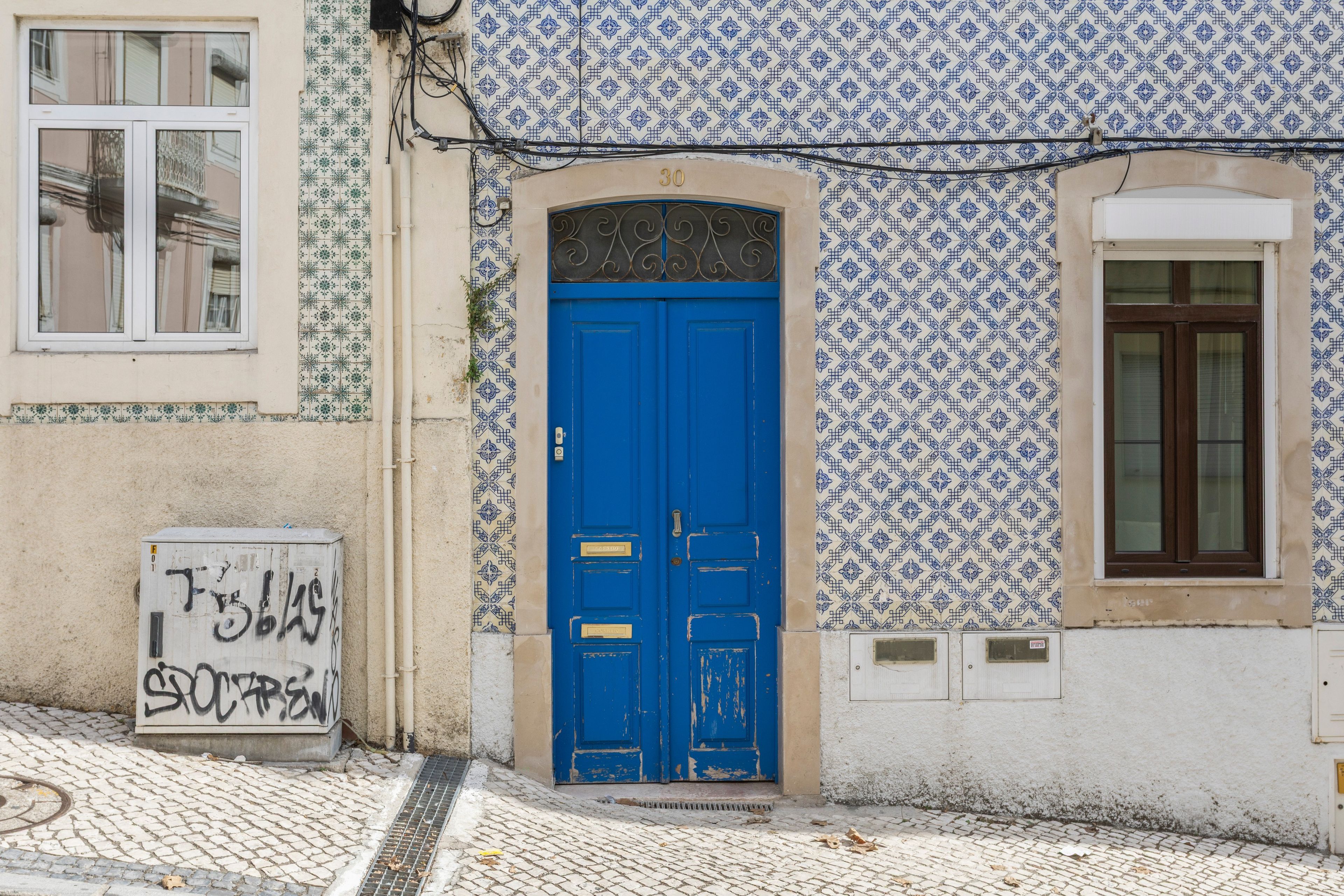 Un edificio con puerta azul, baldosas estampadas y un cartel con grafiti.