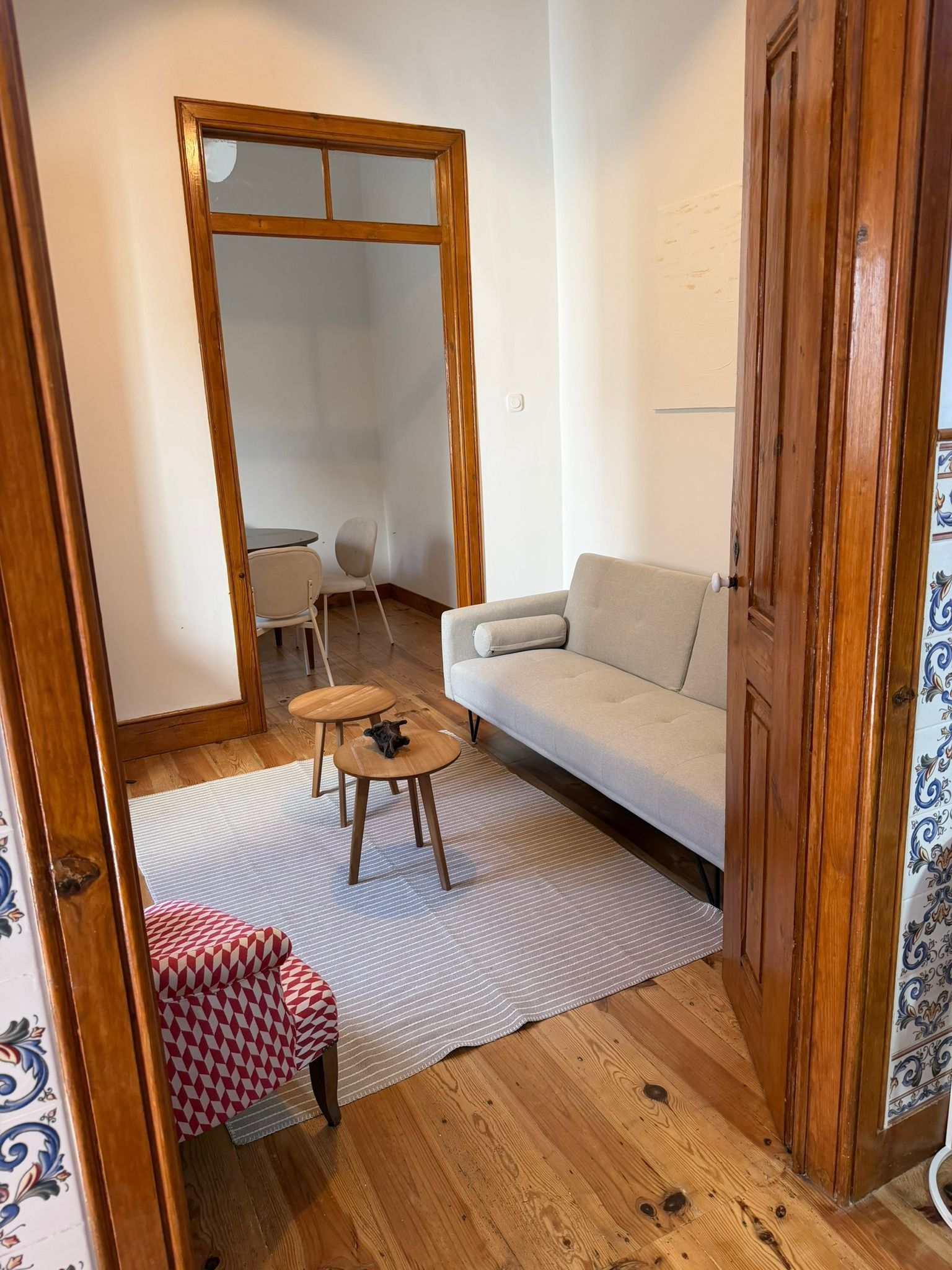 A room with a sofa, a small round table, a chair, a patterned rug, and a large mirror.