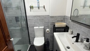 Ein Badezimmer mit Duschkabine, Toilette, Waschbecken mit Spiegel und Handtuchhalter.