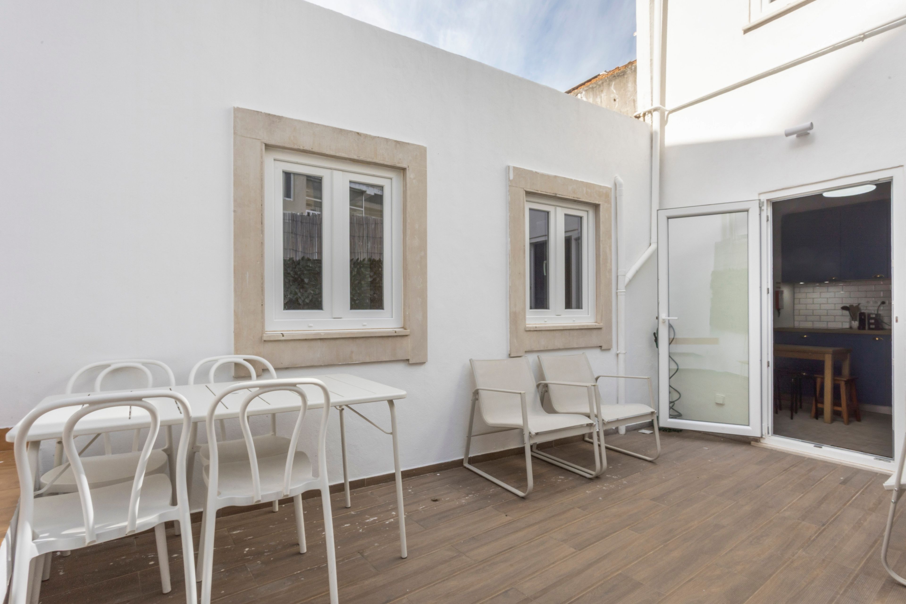 A patio area with a table and chairs, two windows, and a sliding glass door leading to a kitchen.