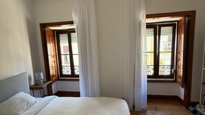 Ein Schlafzimmer mit einem großen Bett, zwei Vorhängen und Holzfußboden sowie einem kleinen Nachttisch.