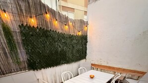 Eine Terrasse im Freien mit einem weißen Tisch und Stühlen, einer weißen Bank und einer dekorativen Wand mit Beleuchtung.
