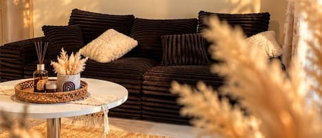 Una sala acogedora con un sofá marrón oscuro, una mesa redonda de centro y un tapiz de macramé en la pared.