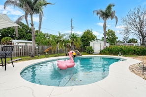 A swimming pool with a pink flamingo float, surrounded by palm trees and a wooden fence. - 2416 Dunbar Avenue (Melbourne)
