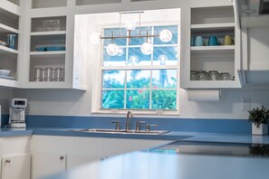 A kitchen with a window, shelves with glassware, a coffee maker, and a sink. - 212 Surf Road (Melbourne Beach)