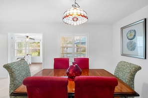 A dining area with a wooden table, red upholstered chairs, a hanging glass chandelier, and a framed botanical illustration on the wall. - 212 Surf Road (Melbourne Beach)