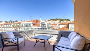 Ein Balkon mit Gartenmöbeln, freier Blick auf eine Stadtansicht mit Gebäuden und einer Hügelkulisse im Hintergrund.