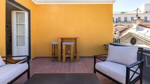 A balcony with a yellow wall, a wooden table with two chairs, and a sofa. - Chiado Terrace & Castle View 2BR by LovelyStay (Lisboa)