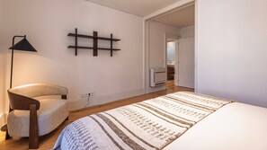 Ein Schlafzimmer mit einem Bett, einem Sessel, einer Lampe und einem an der Wand befestigten Regal.