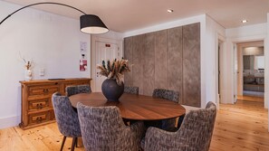 A modern dining area with a round wooden table, upholstered chairs, a vase with dried plants, and a pendant light. - Chiado Terrace & Castle View 2BR by LovelyStay (Lisboa)