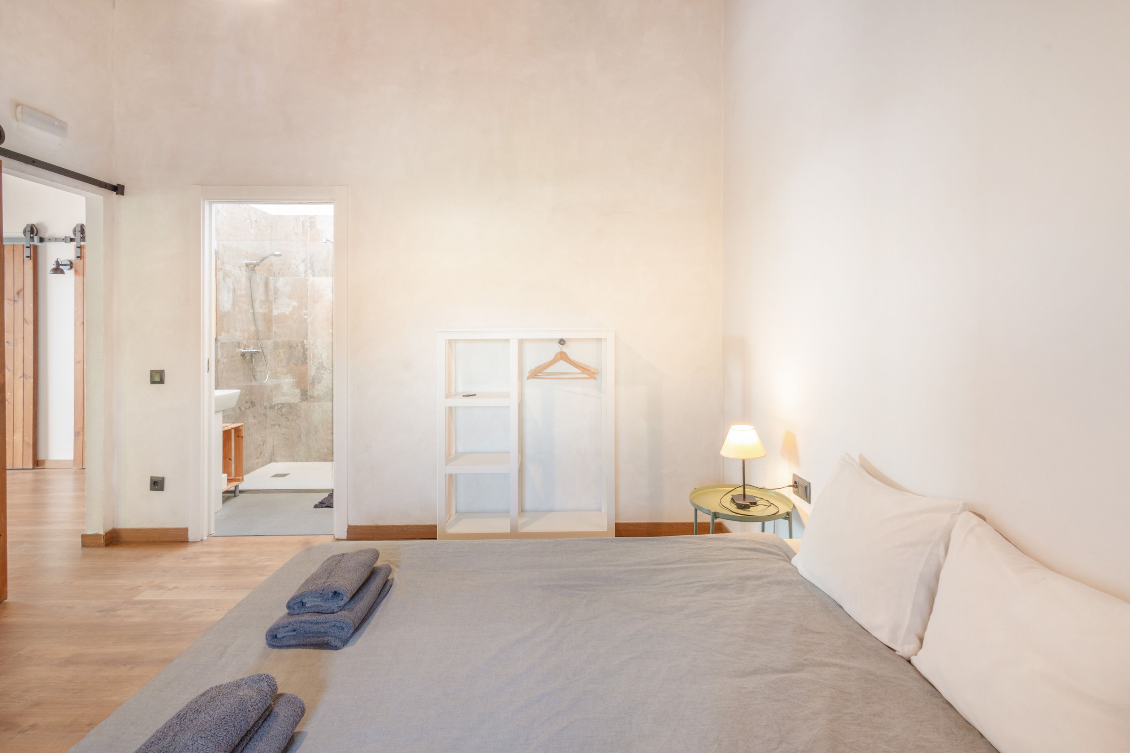 Un dormitorio amplio con una cama grande, una mesita de noche con lámpara y un armario con barra para colgar.