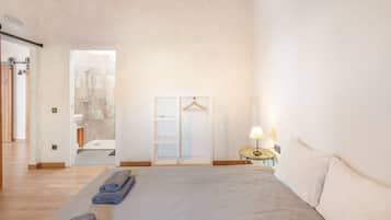 Un dormitorio amplio con una cama grande, una mesita de noche con lámpara y un armario con barra para colgar.