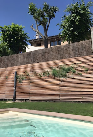 A swimming pool with a wooden deck and a stone wall. - Country House 'Casa Rural Del 1900 En Vall Del Ges' with Mountain View, Wi-Fi and Air Conditioning (Sant Vicenç de Torelló)