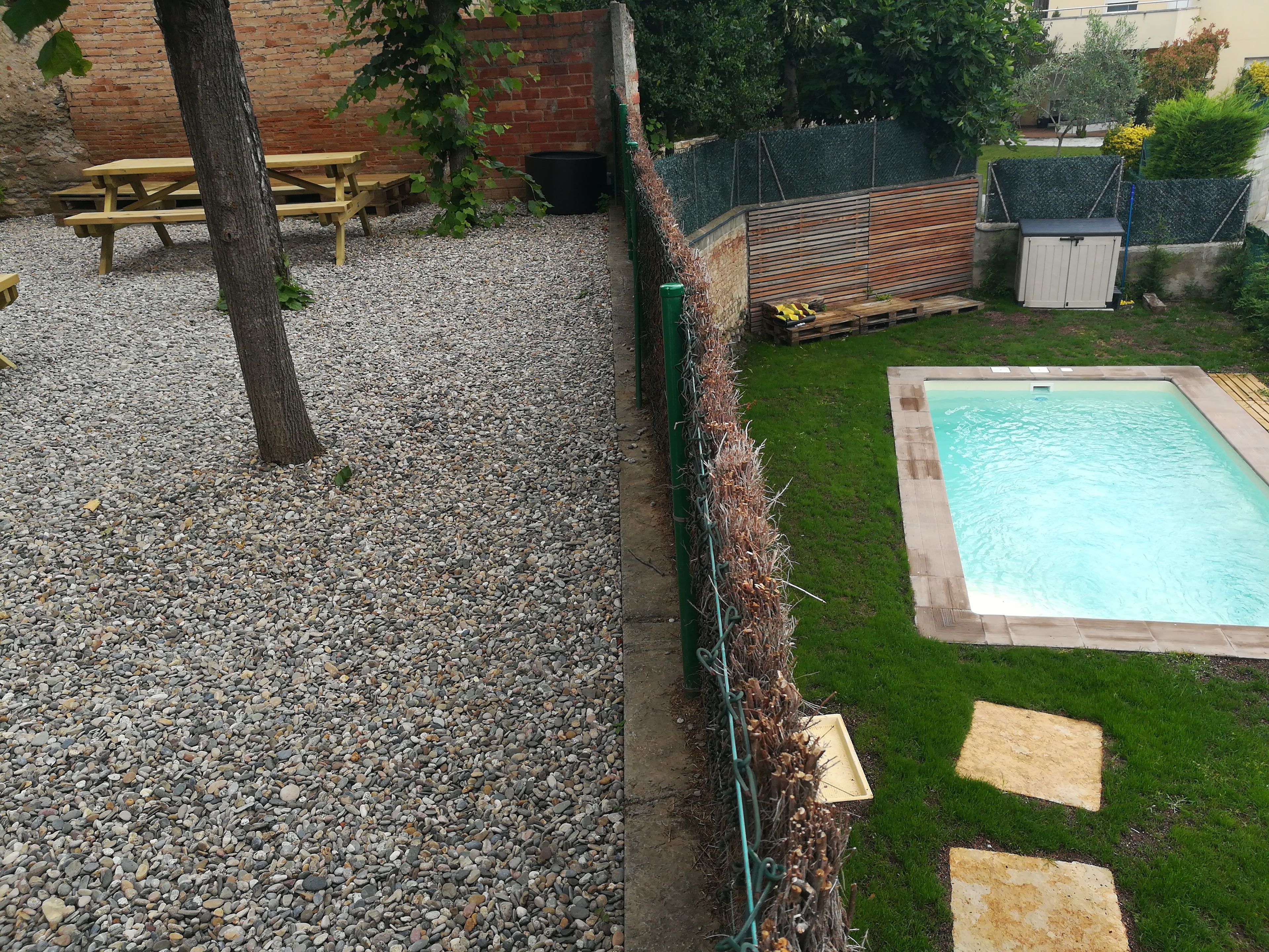 Un patio trasero con piscina, un banco de madera y un muro de ladrillo.