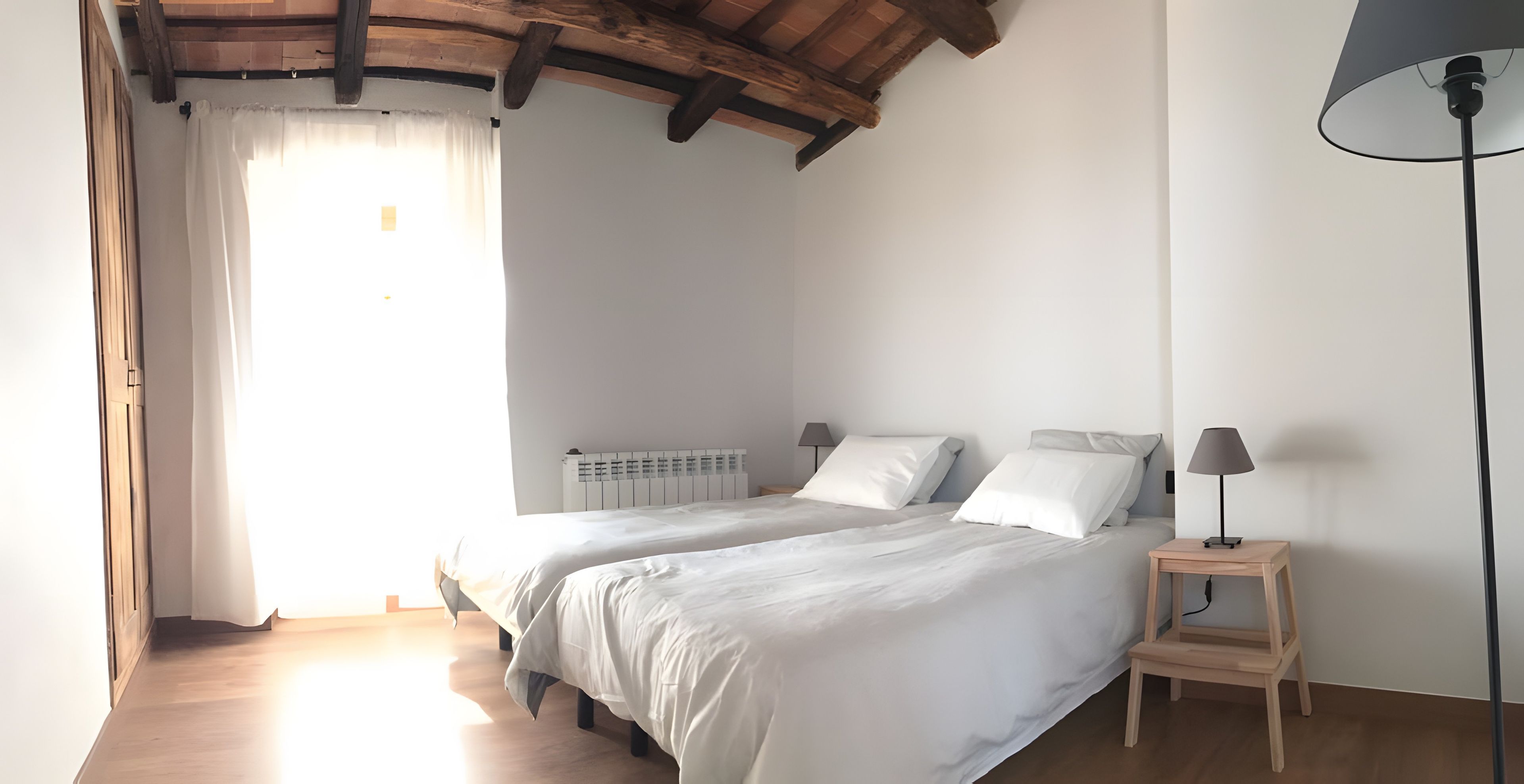 Un dormitorio con dos camas, piso de madera, un radiador y una lámpara.