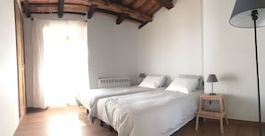 A bedroom with two beds, a wooden floor, a radiator, and a lamp.
