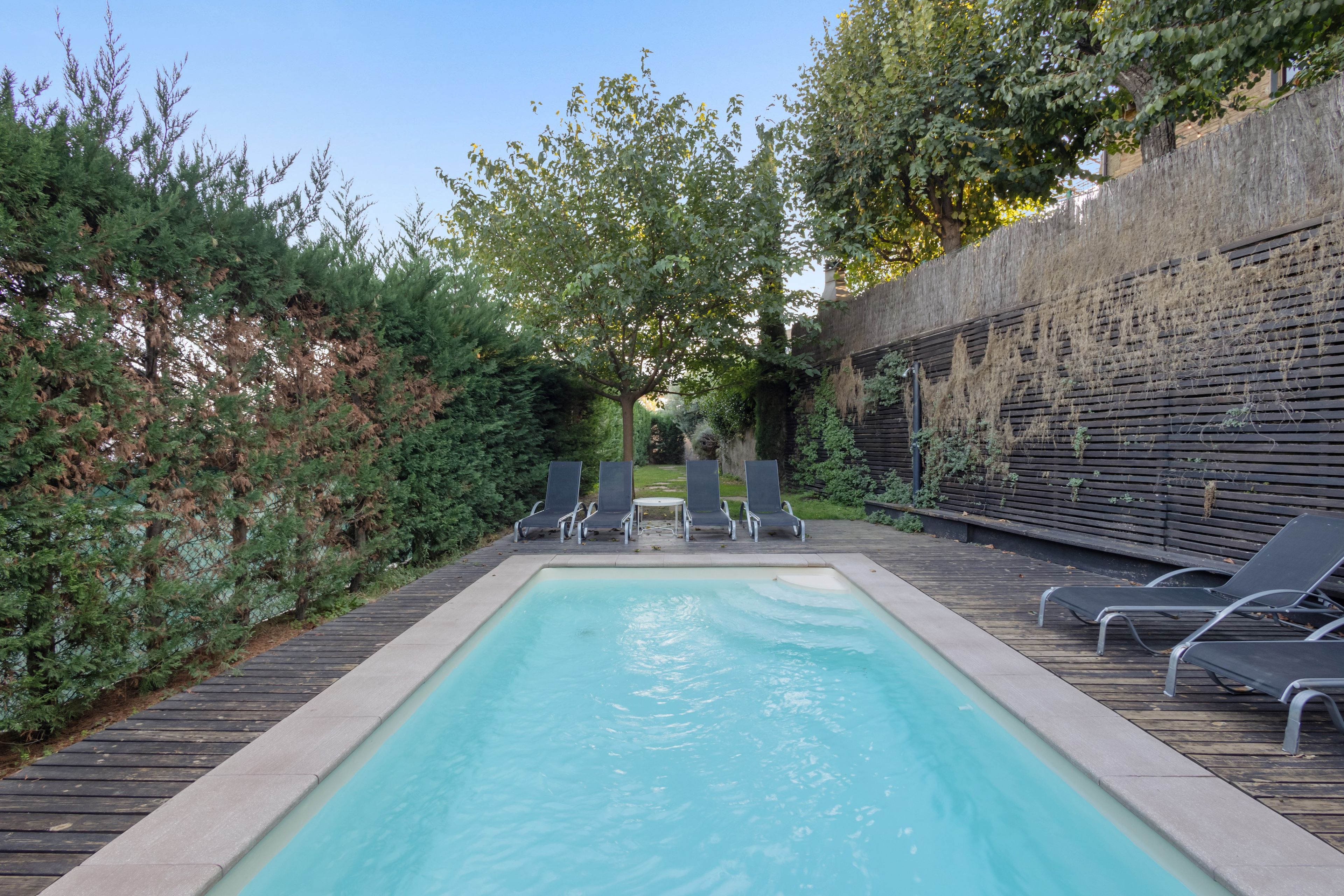 Una piscina rectangular con un deck de madera alrededor, equipada con sillones de descanso.