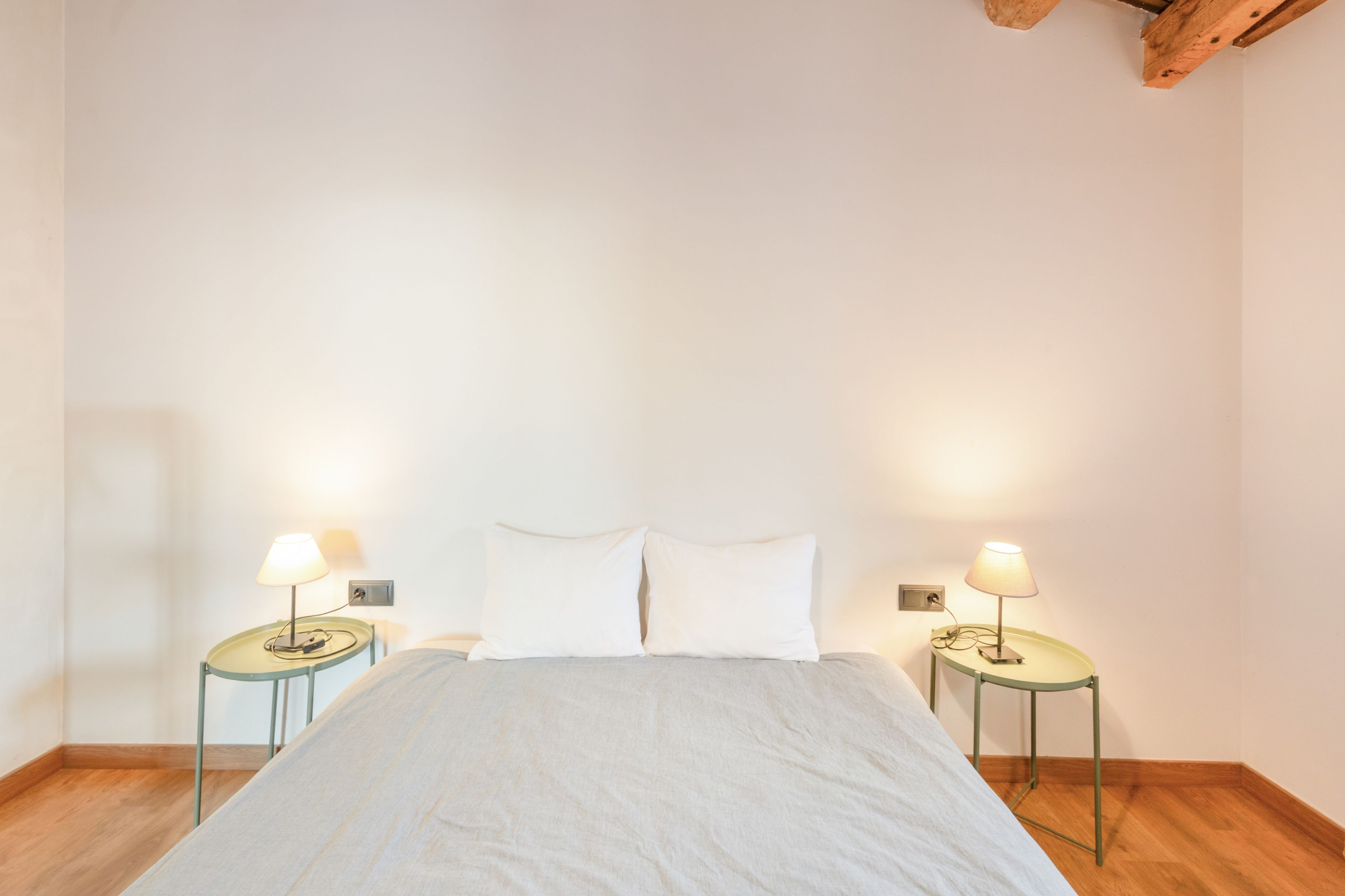 Un dormitorio con cama, dos mesitas de noche con lámparas y una viga de techo de madera.