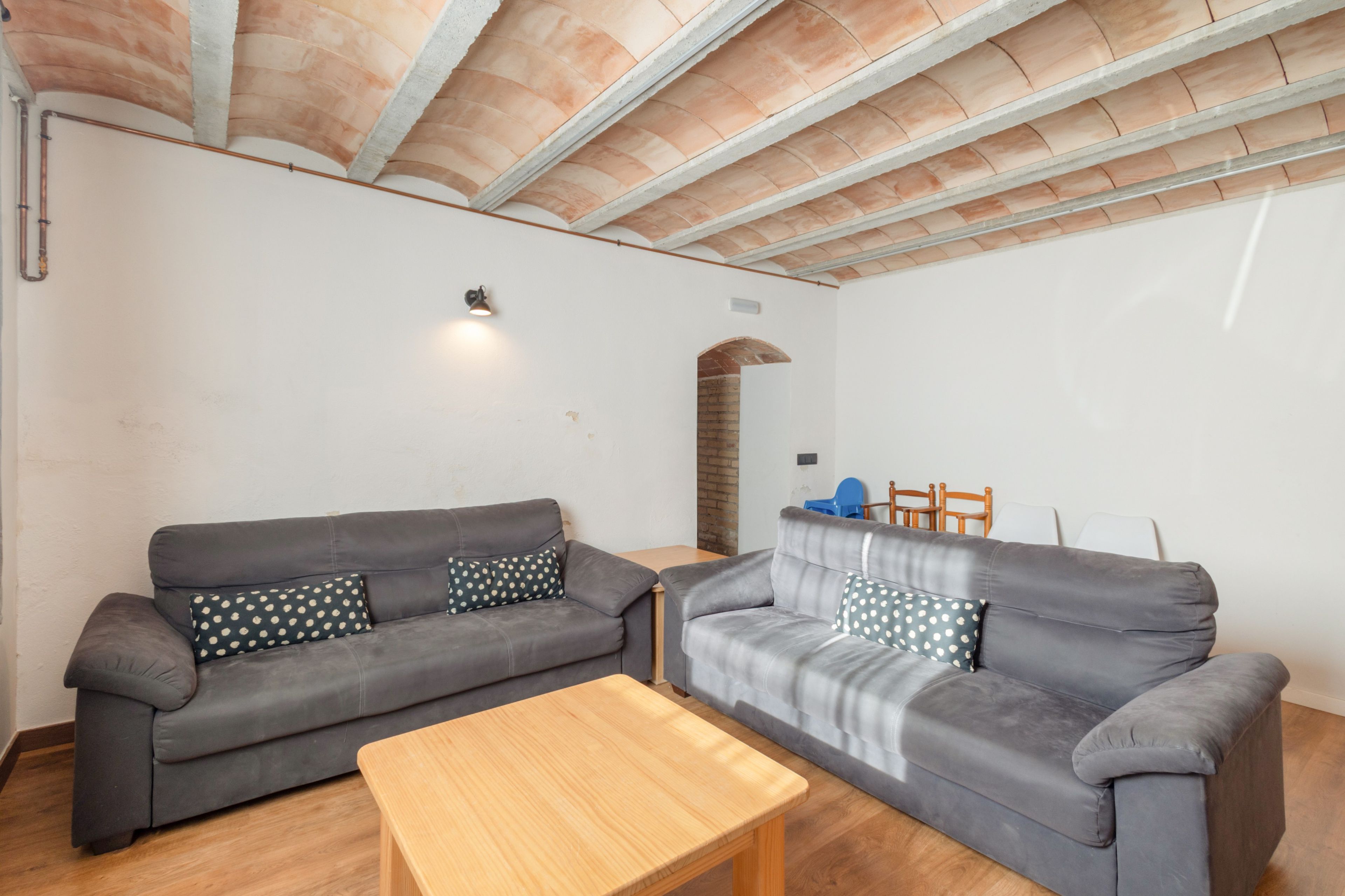 A living room with two grey sofas, a wooden coffee table, and a brick archway leading to another room.