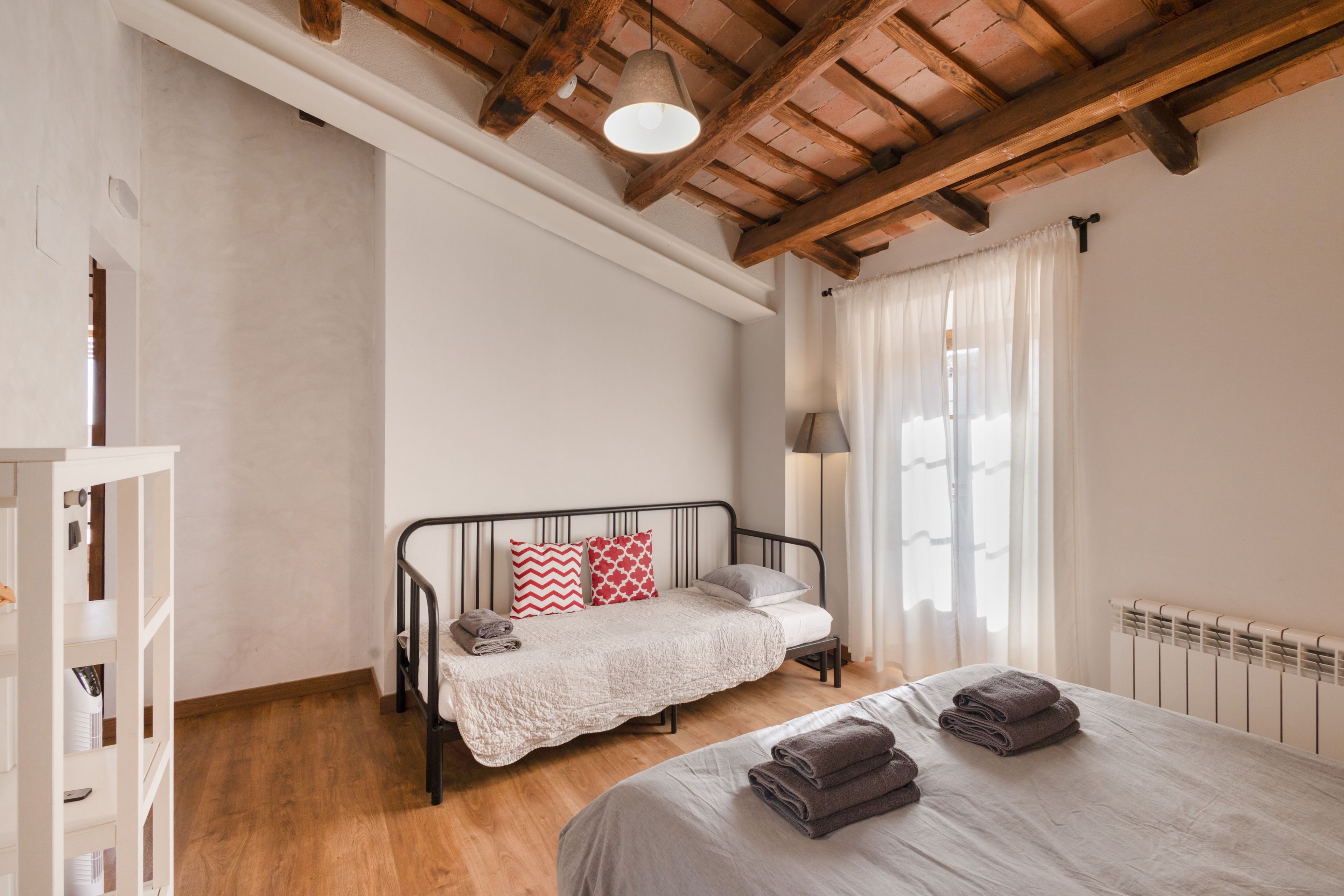 Un dormitorio con cama, mesita de noche, lámpara y ventana con cortinas.